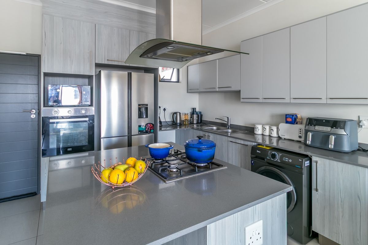 Modern kitchen featuring light wood-grain cabinetry, stone countertops, a central island with a gas hob, and integrated stainless steel appliances.