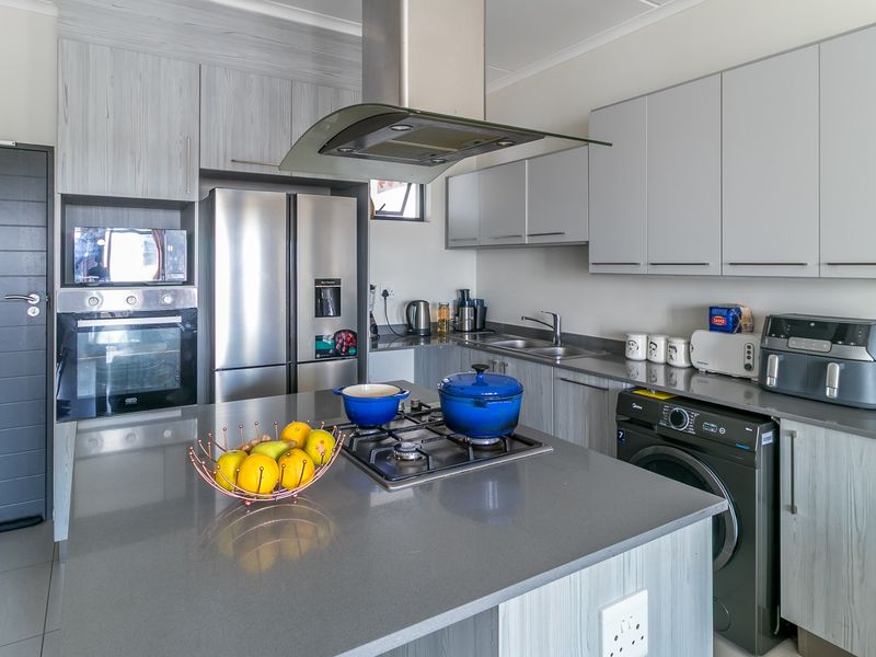 Modern kitchen featuring light wood-grain cabinetry, stone countertops, a central island with a gas hob, and integrated stainless steel appliances.