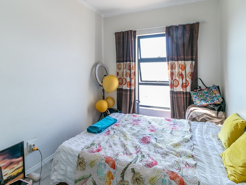A compact bedroom featuring neutral walls, a window with curtains, and standard electrical fixtures.
