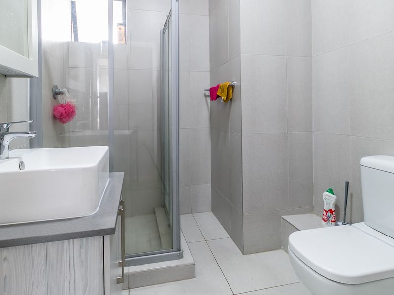 A clean, modern bathroom featuring a glass shower enclosure, a contemporary vanity with basin, and a standard toilet with neutral wall and floor tiling.