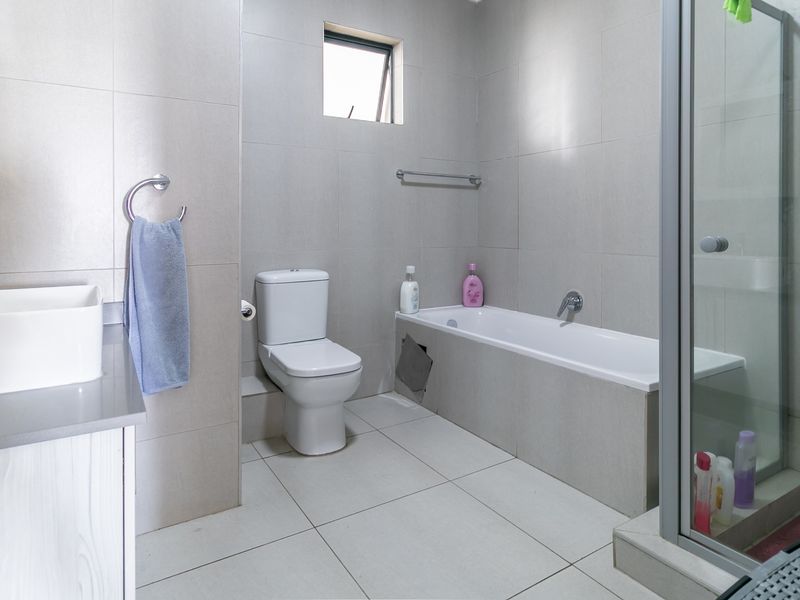 A functional bathroom featuring a vanity, toilet, bathtub, and separate shower enclosure with neutral wall and floor tiling.