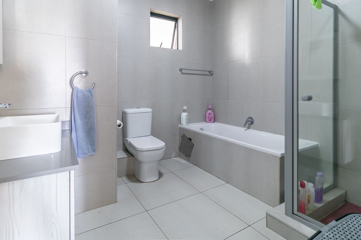 A functional bathroom featuring a vanity, toilet, bathtub, and separate shower enclosure with neutral wall and floor tiling.