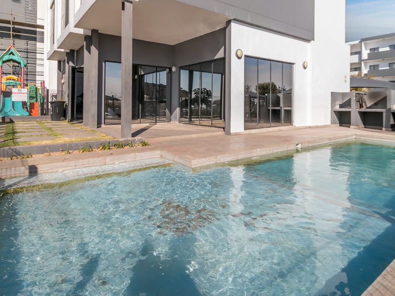 Outdoor pool area featuring a swimming pool, paved patio, and built-in braai facilities, adjacent to the apartment building's sliding glass doors.