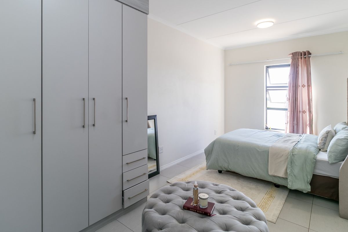 A well-maintained bedroom featuring neutral tiled flooring, ample built-in cupboard storage, and natural light from a top-hung window.