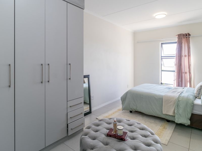 A well-maintained bedroom featuring neutral tiled flooring, ample built-in cupboard storage, and natural light from a top-hung window.