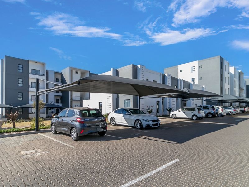 Exterior view of a modern apartment complex featuring paved parking bays with shade cloth carports.