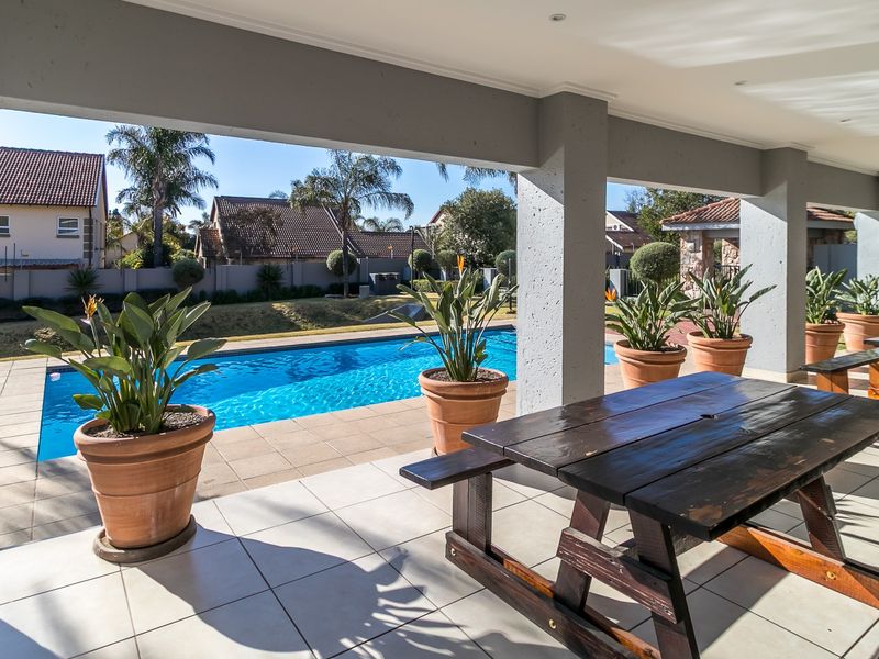 A spacious covered patio featuring tiled flooring and recessed lighting, overlooking a well-maintained swimming pool and garden area.