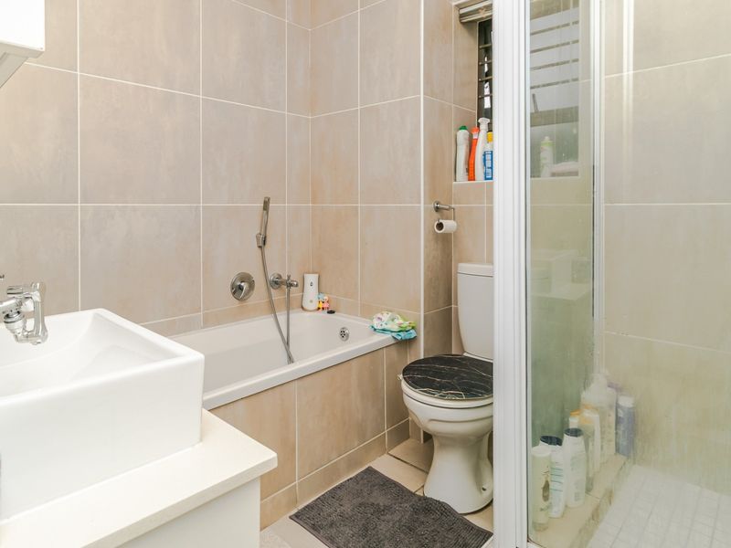 Compact bathroom featuring a built-in bathtub, separate shower enclosure, wall-mounted basin, and toilet with neutral ceramic wall tiling.