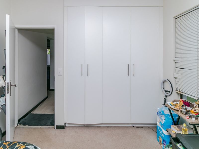 A bedroom featuring white built-in cupboards and a window with venetian blinds, providing functional storage and natural light.