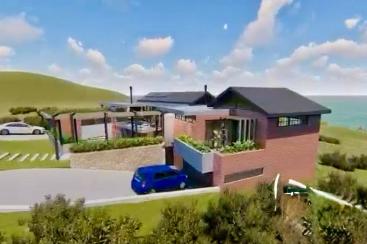 An aerial view of a modern brick residential property featuring a pitched roof, landscaped garden, and paved driveway, situated in a coastal setting.
