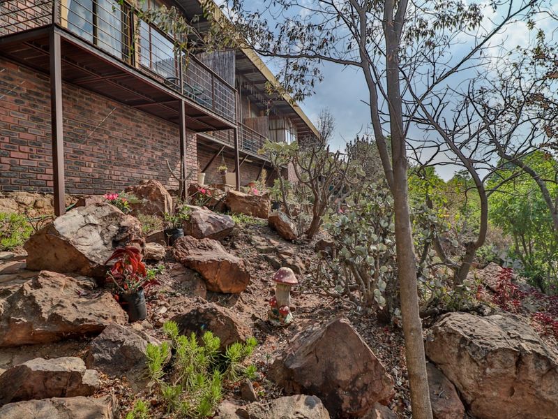 A rear view of the property featuring a brick facade with an elevated metal balcony overlooking a natural rock garden.