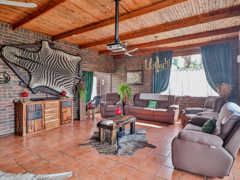 Spacious living room featuring exposed brick walls, a high timber-beamed ceiling, and durable ceramic tile flooring, creating a rustic and warm atmosphere.