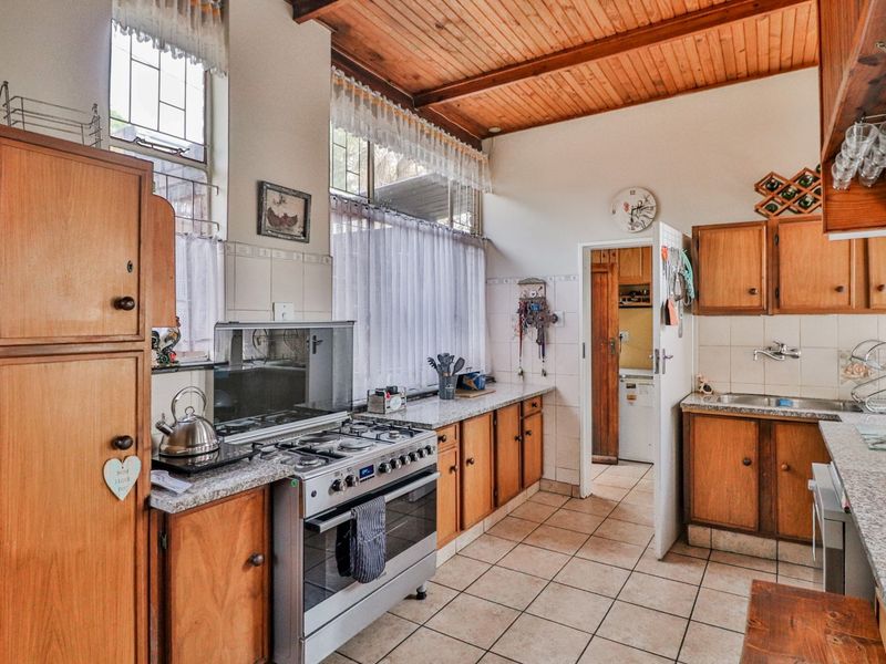 A functional kitchen featuring wooden cabinetry, granite countertops, a gas stove, and a timber ceiling, with direct access to a scullery area.