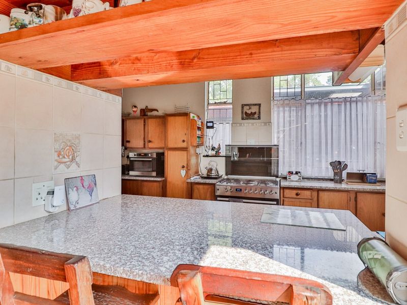 A functional kitchen featuring granite countertops, wooden cabinetry, a gas stove, and exposed timber ceiling beams, offering a classic, lived-in aesthetic.