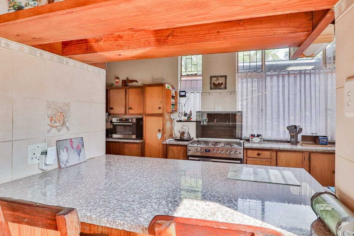 A functional kitchen featuring granite countertops, wooden cabinetry, a gas stove, and exposed timber ceiling beams, offering a classic, lived-in aesthetic.