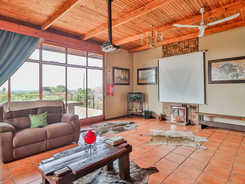 Spacious living room featuring a rustic exposed timber ceiling, terracotta tiled flooring, and a wood-burning fireplace, with large glass doors opening to a balcony.