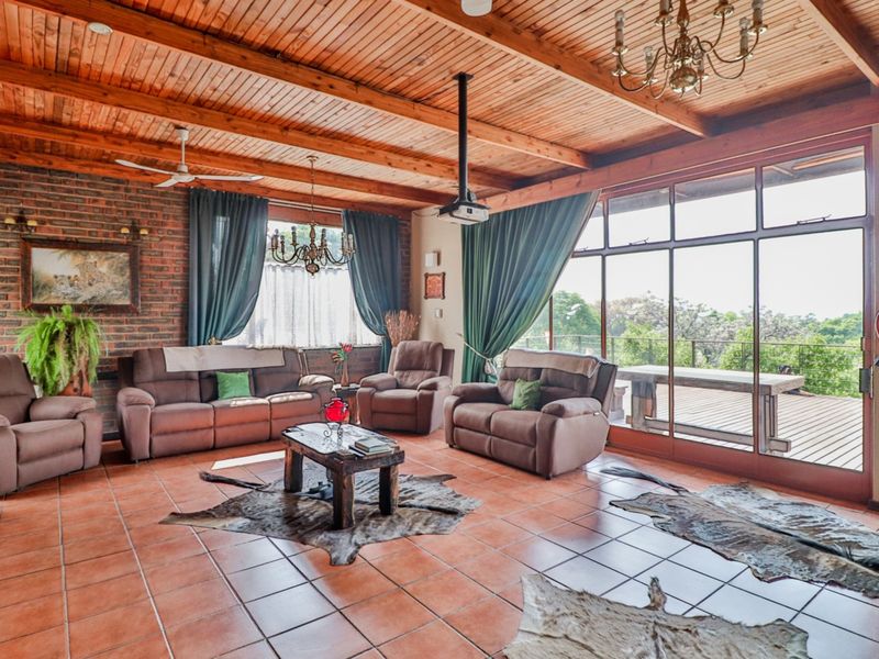 Spacious living room featuring exposed timber beam ceilings, terracotta floor tiles, an exposed brick feature wall, and large glass doors opening to a deck.