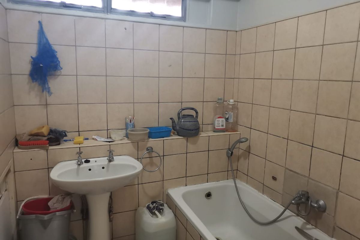 A dated bathroom featuring a pedestal basin, a built-in bathtub with a handheld shower attachment, and full-height wall tiling.