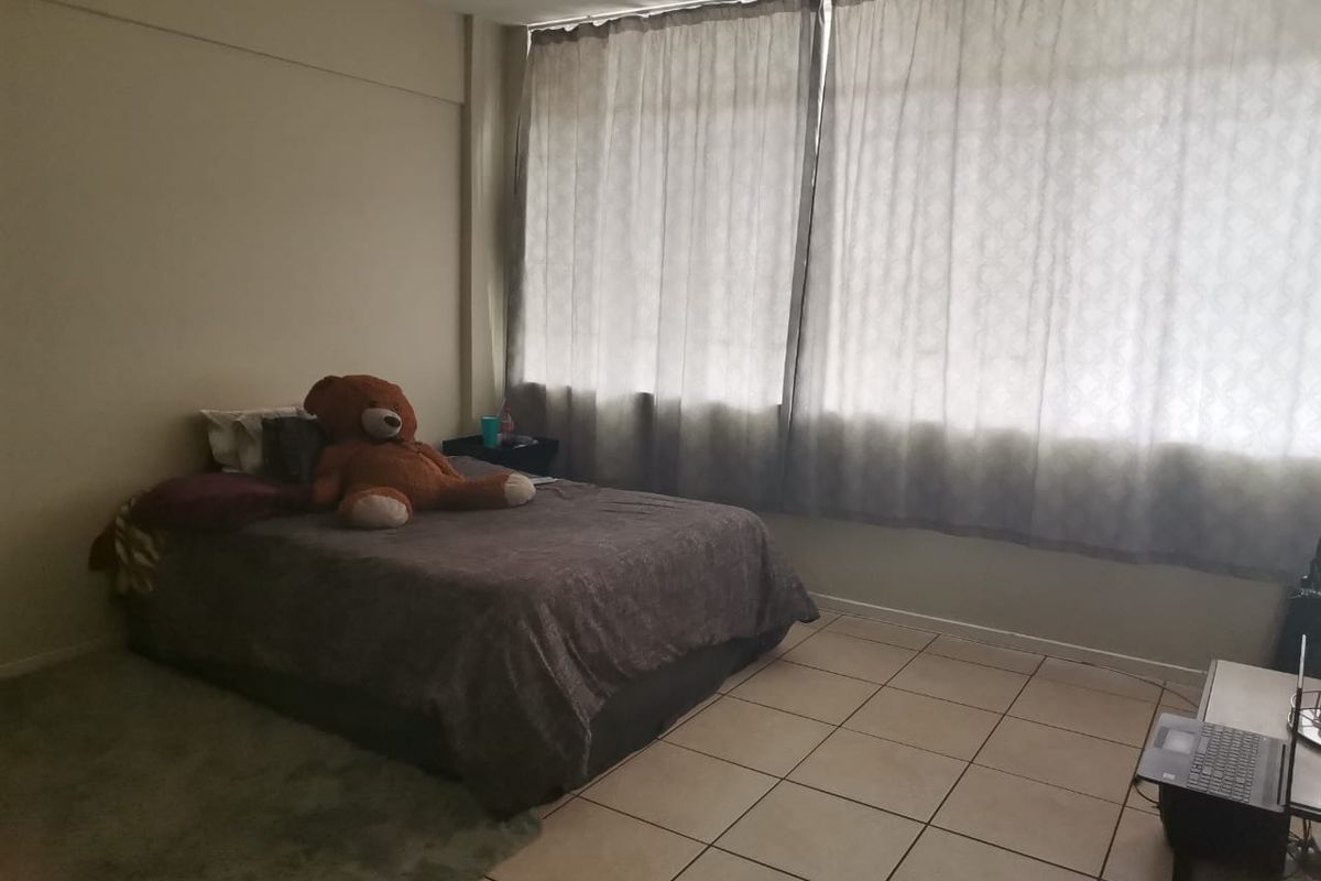 A bedroom featuring tiled flooring and large windows with curtains, providing natural light to the space.