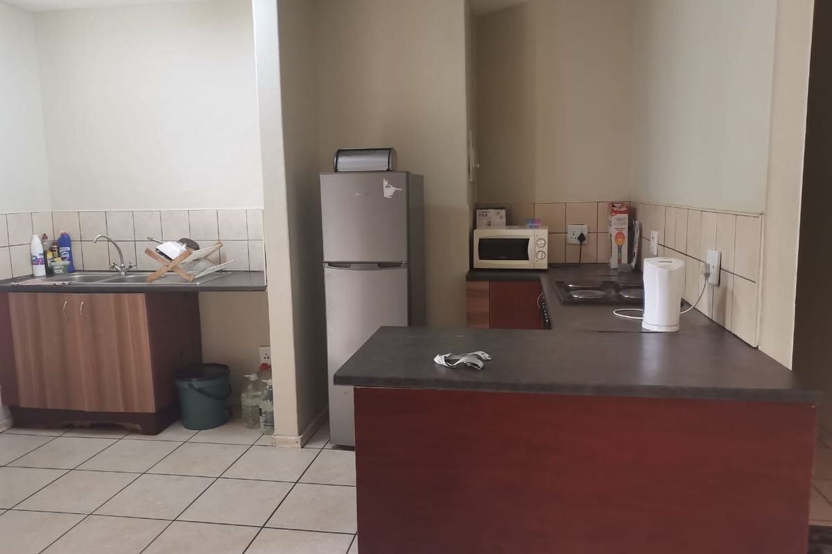 Functional kitchen area featuring laminate countertops, built-in cabinetry, tiled splashbacks, and a dedicated sink area with tiled flooring.