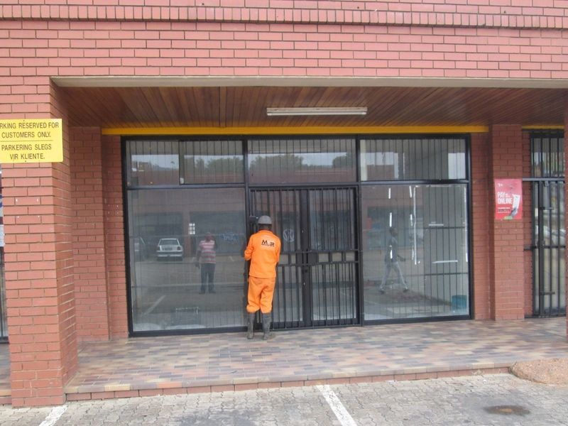 Front exterior view of a commercial office or retail space featuring a brick facade, glass storefront, and secure metal gate entrance.