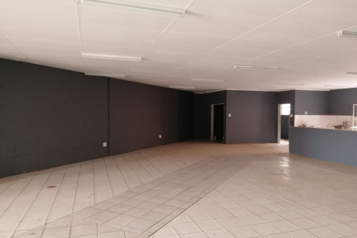 Spacious open-plan office area featuring tiled flooring, a suspended ceiling with integrated lighting, and a built-in counter section.