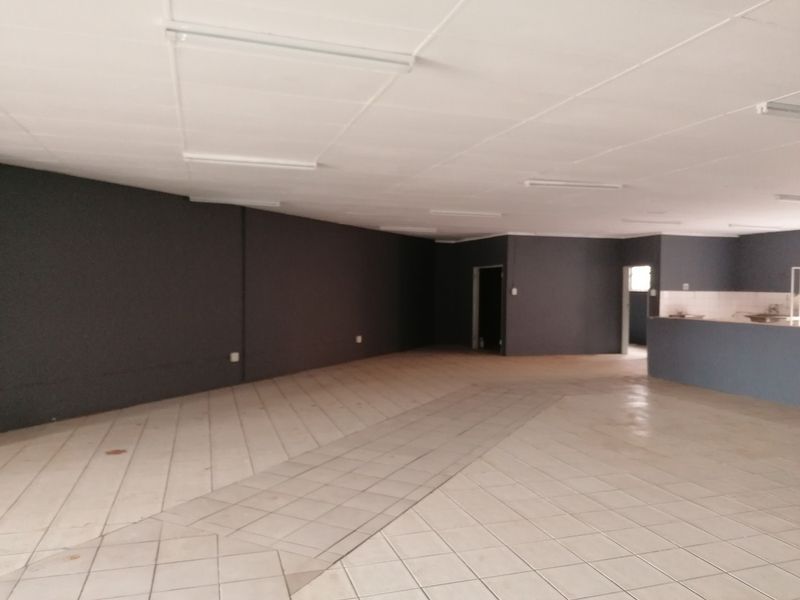 Spacious open-plan office area featuring tiled flooring, a suspended ceiling with integrated lighting, and a built-in counter section.