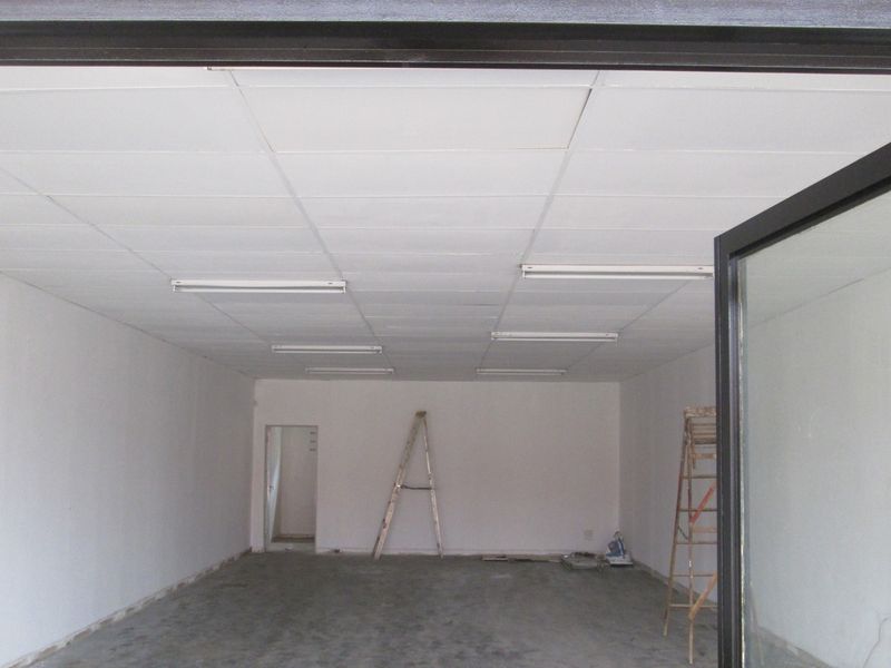 An empty office space featuring a suspended ceiling with integrated fluorescent lighting and a glass entrance door, currently in a shell condition.