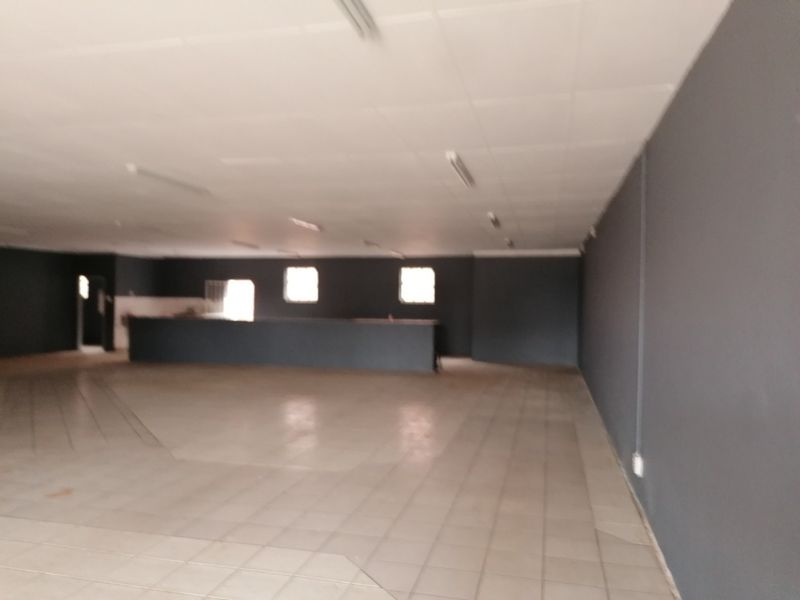 A large, empty open-plan office space featuring tiled flooring, a suspended ceiling with fluorescent lighting, and a built-in service counter.