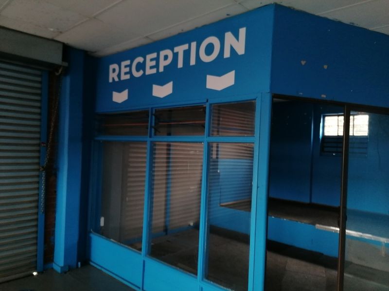 An empty office reception area featuring blue painted partitions, glass paneling, and a roller shutter door, suitable for commercial use.