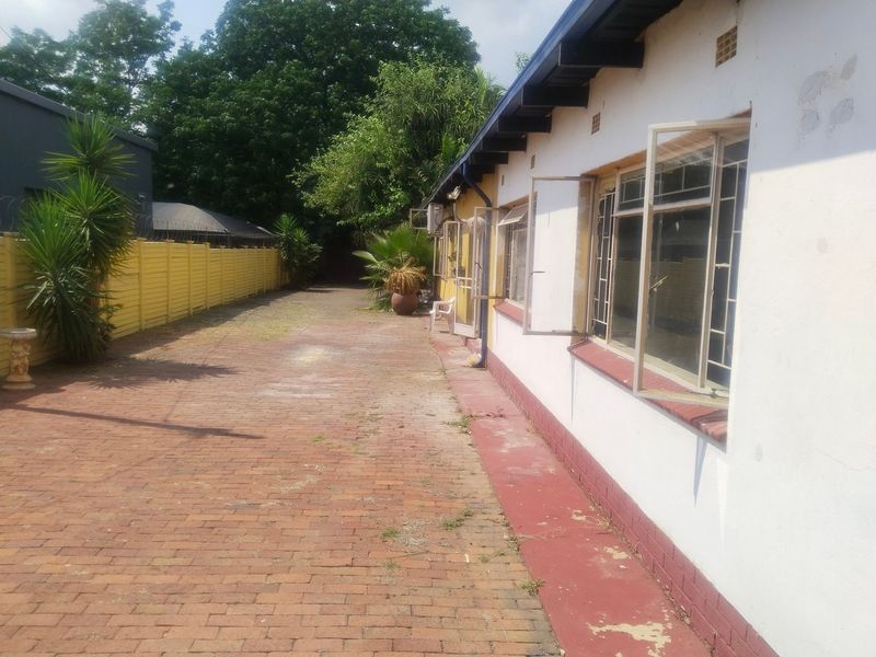 Rear exterior view of the office building featuring brick paving, steel window frames, and a boundary wall with visible signs of wear.