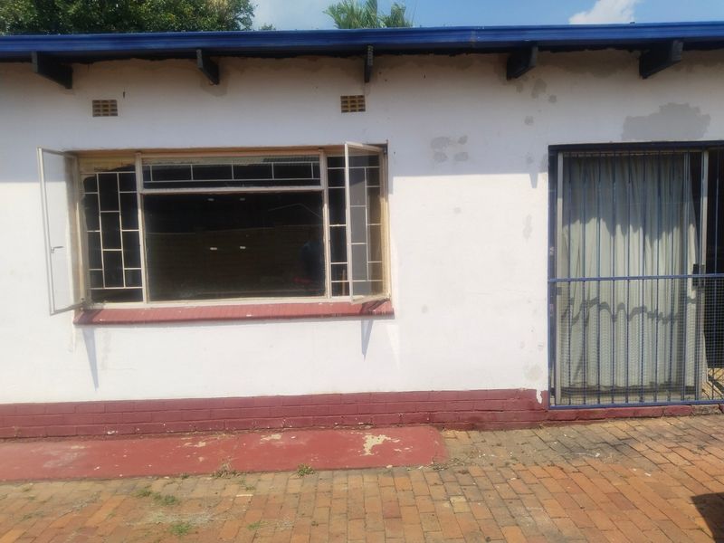 Exterior view of the office building featuring steel window frames, a security gate, and paved ground area with visible wear to the exterior paintwork.