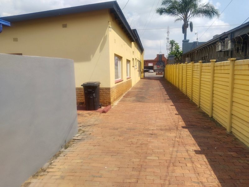 A paved side access driveway featuring a precast concrete boundary wall with security razor wire and a metal gate.