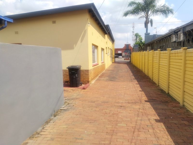 A paved side access path between the office building and a perimeter wall, featuring security fencing and a gated entrance.