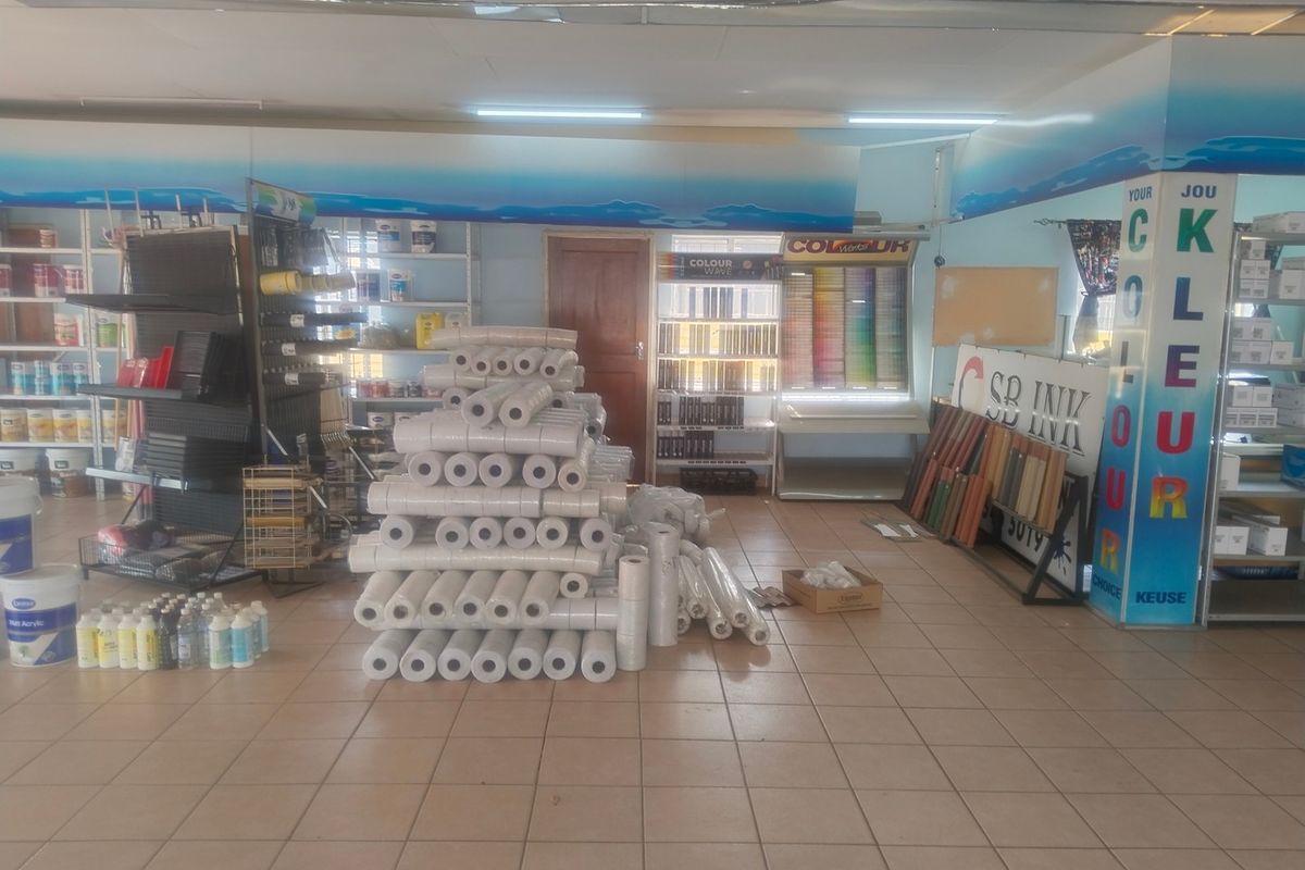 A commercial office or retail space featuring tiled flooring, built-in shelving, and overhead fluorescent lighting, currently utilized for product storage and display.