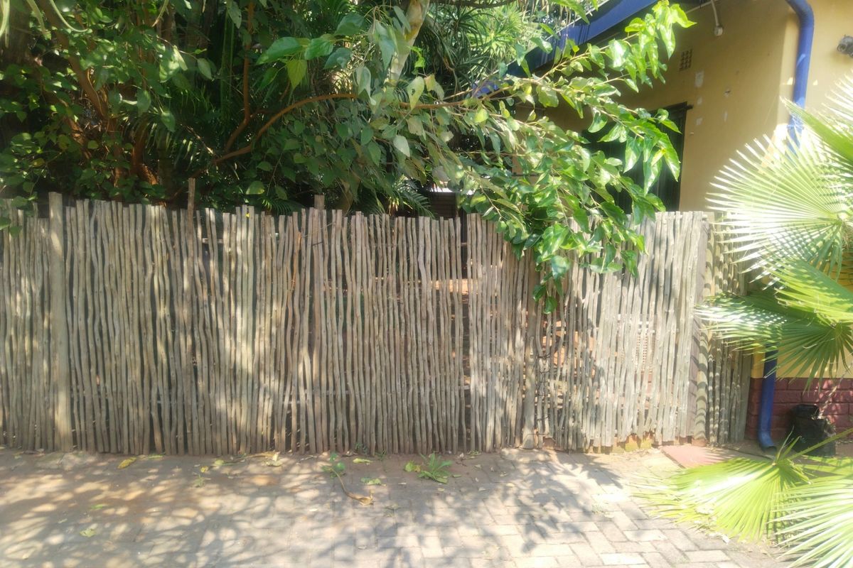 A view of the rear exterior area featuring a timber pole fence and paved ground surface.
