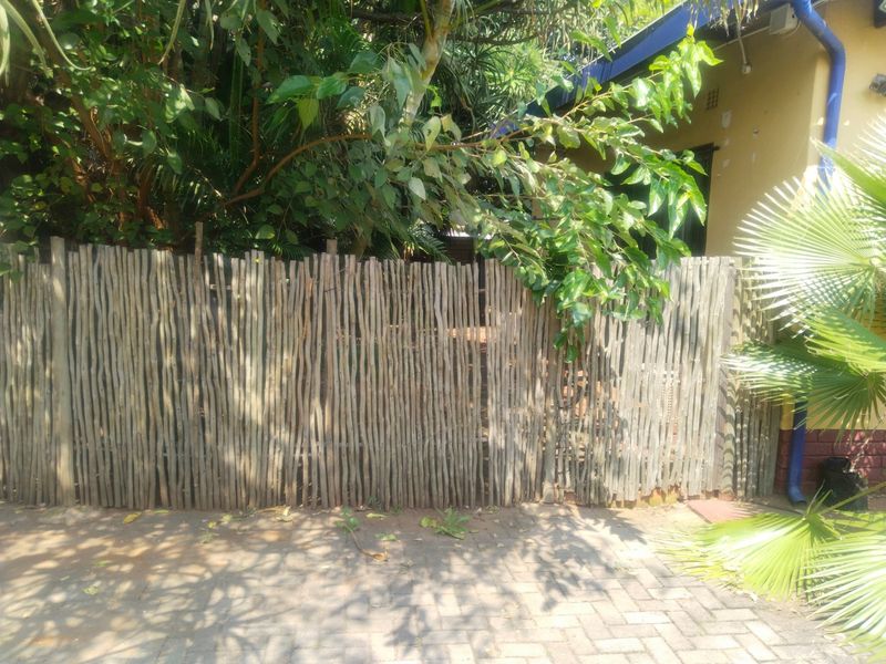 A view of the rear exterior area featuring a timber pole fence and paved ground surface.