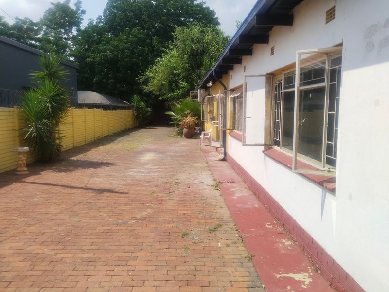 Rear exterior view of the office building featuring a brick-paved pathway, perimeter wall with security spikes, and multiple casement windows.