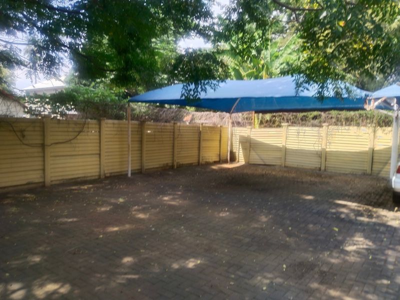 A paved outdoor parking area featuring a blue shade cloth carport structure and enclosed by a perimeter boundary wall.