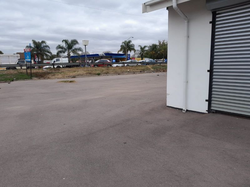 Exterior view of a commercial property featuring a roller shutter door and an asphalt parking area.