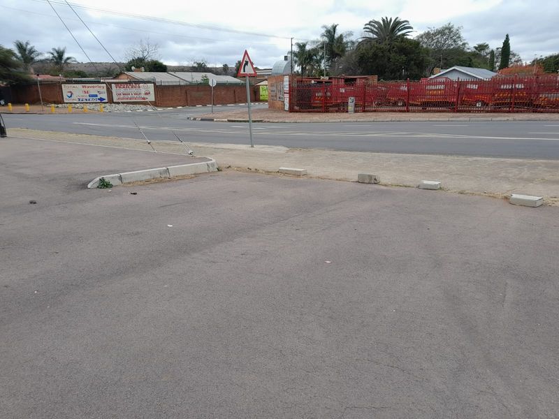 Street-level view of the property frontage showing an asphalt parking area, perimeter fencing, and adjacent road infrastructure.