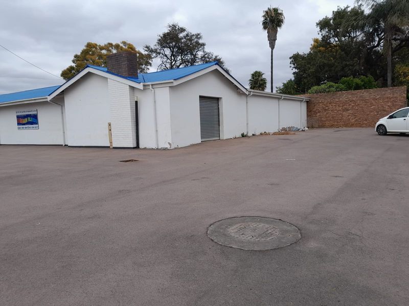 Rear exterior view of a commercial property featuring an asphalt parking area, a roller shutter door, and a brick boundary wall.