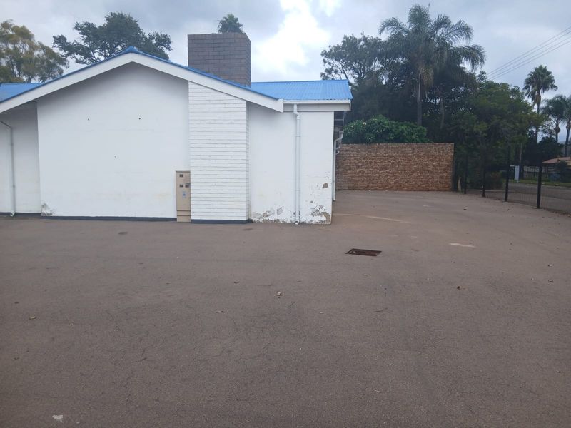 Rear exterior view of the property featuring an asphalt parking area, brick chimney, and painted masonry walls showing signs of wear.