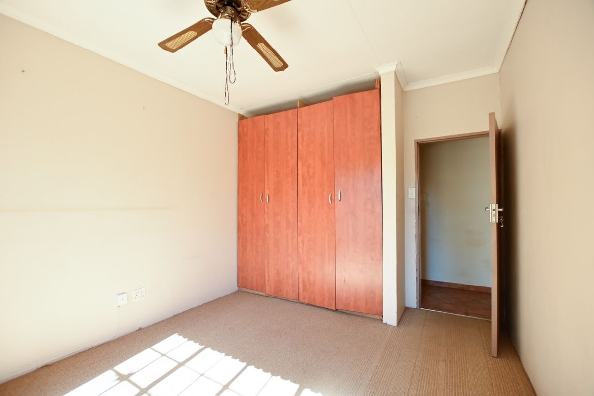 An empty bedroom featuring built-in wooden cupboards, a ceiling fan, and carpeted flooring, offering a blank canvas for office or residential use.
