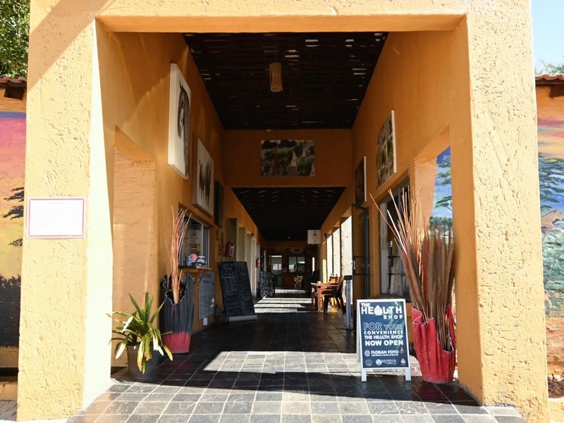 A covered outdoor entrance walkway featuring textured stucco walls, tiled flooring, and an exposed timber beam ceiling, leading into the office complex.