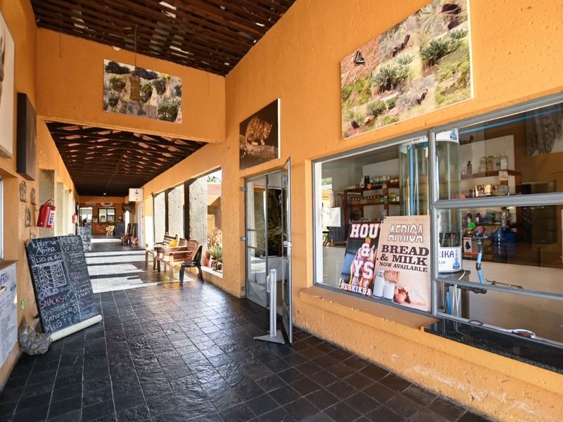 A covered outdoor walkway or patio area featuring tiled flooring, exposed timber beams, and large display windows suitable for retail or office frontage.