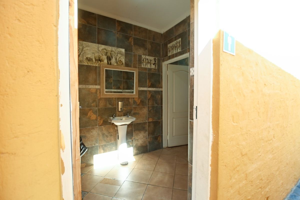 A functional office bathroom featuring tiled walls, a pedestal basin, and a wall-mounted soap dispenser.