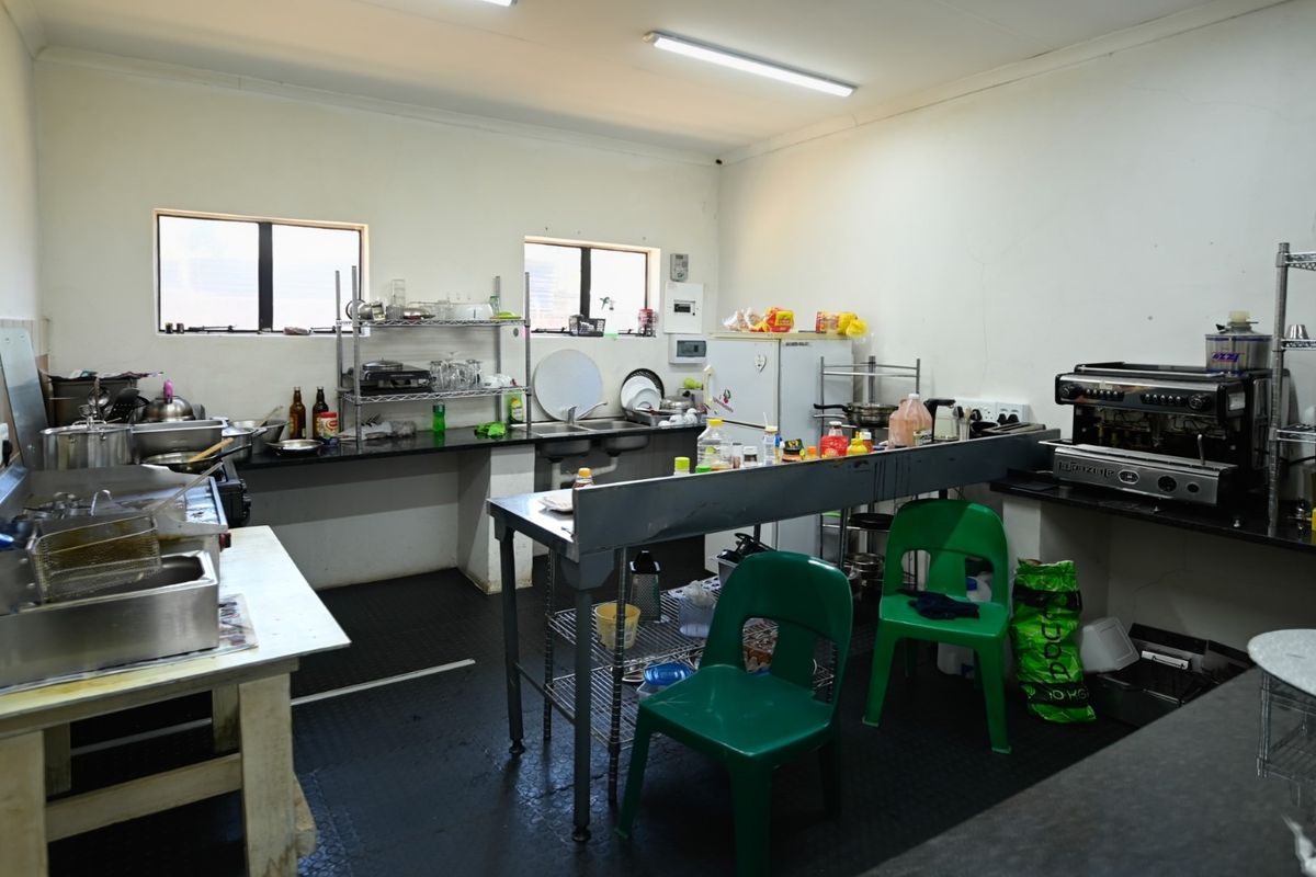 A functional commercial kitchen space featuring black granite countertops, a double sink, and durable rubber flooring, suitable for office or cafe operations.