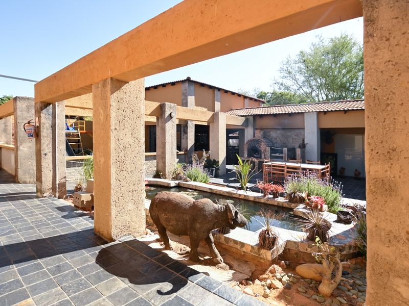 Spacious covered patio area featuring a built-in braai, stone-lined water feature, and durable tiled flooring, ideal for outdoor office relaxation or client entertainment.