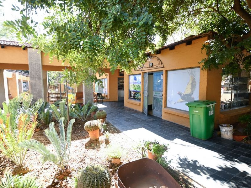 A view of the rear exterior office area featuring a covered walkway, tiled flooring, and established garden landscaping.